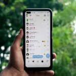 A hand holding a smartphone displaying a chat application outdoors against a green background.